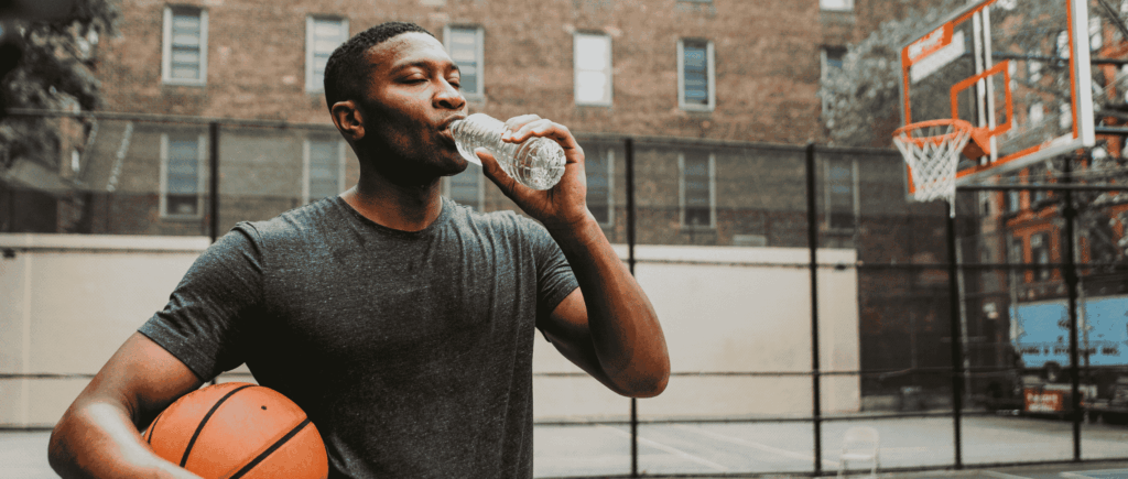 Young man drinking from a water bottle on a basketball court